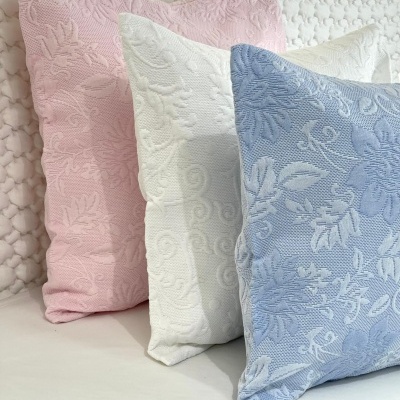 Três almofadas decorativas em rosa, branco e azul com padrões florais texturizados
