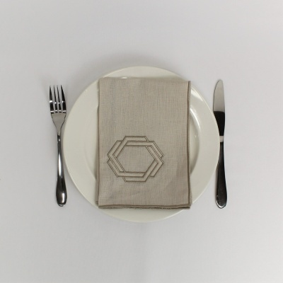 Prato branco com guardanapo bege bordado, garfo e faca metálicos lado a lado