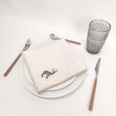 Mesa posta com talheres de madeira e metal, prato branco, guardanapo bege com bordado de veado e copo de vidro