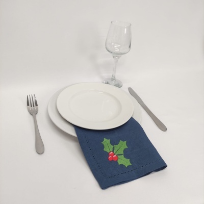 Mesa posta minimalista com prato branco, guardanapo azul bordado, talheres de metal e copo de vidro.