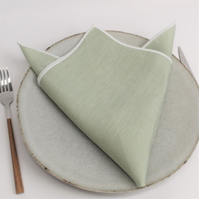 Guardanapo verde claro com borda branca sobre prato cinzento, garfo com cabo castanho ao lado