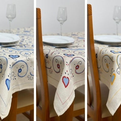 Três toalhas de mesa com padrões de corações e arabescos em três cores diferentes sobre uma mesa de madeira