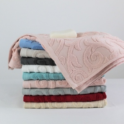 Pilhas de toalhas de algodão coloridas com padrões em relevo espiralados num fundo neutro