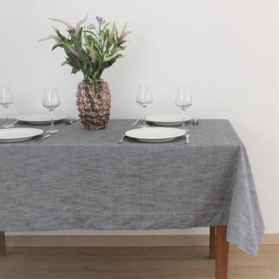 Mesa com toalha cinzenta, vaso de vidro rosa com flores e conjunto de pratos e copos.