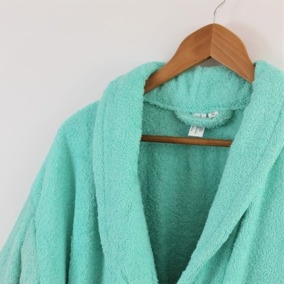 Roupão de banho verde-água de felpa pendurado num cabide de madeira