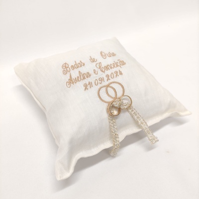Almofada branca com texto bordado dourado e dois anéis dourados com fita de renda