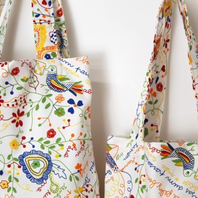 Sacolas de tecido coloridas com padrões de pássaros, flores e texto manuscrito em francês.