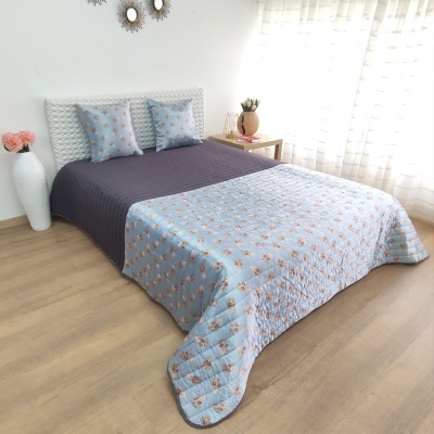 Colcha bicolor com padrão floral e almofadas numa cama branca com piso de madeira clara