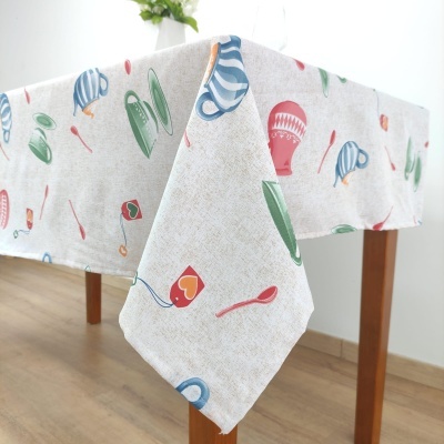 Toalha de mesa bege com padrão colorido de objetos de cozinha sobre mesa de madeira