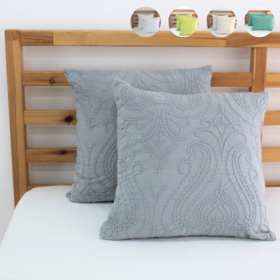 Duas almofadas cinzentas com padrão texturizado sobre cama com cabeceira de madeira