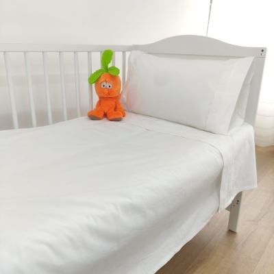 Cama de criança branca com roupa de cama branca e peluche de cenoura laranja
