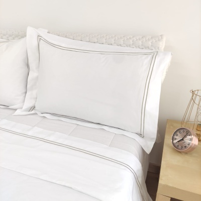 Jogo de cama branco com linhas cinza e relógio numa mesa de cabeceira amarela