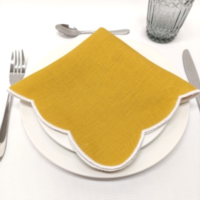 Guardanapo amarelo de tecido com bordas brancas sobre prato branco, com talheres e copo de vidro