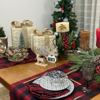 Mesa de Natal com decoração vermelha e preta, pratos brancos e decoração de velas e árvore pequena