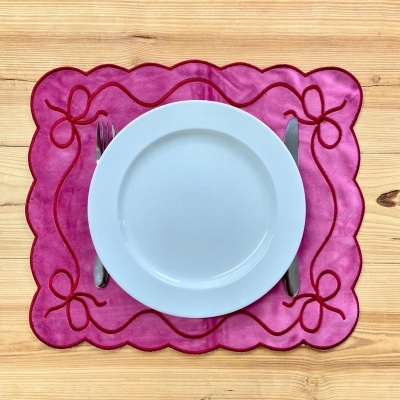 Conjunto de prato branco sobre individual rosa com bordas onduladas e laços vermelhos