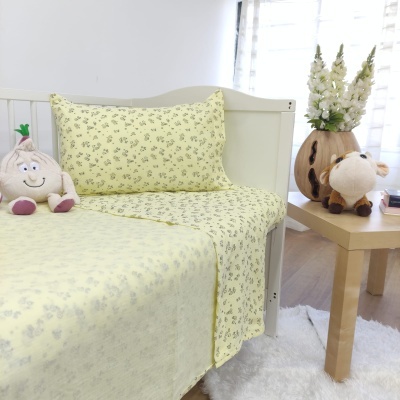 Roupas de cama amarelas com padrão floral num quarto claro com peluches e mesa de madeira