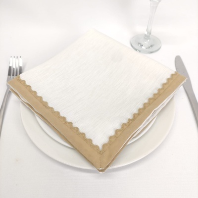 Guardanapo branco com borda bege ondulada sobre prato branco com talheres e taça
