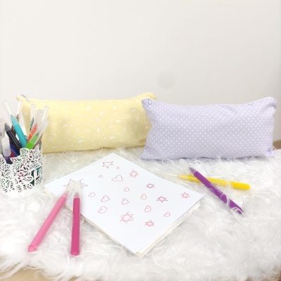 Estojos coloridos, canetas e caderno com desenhos sobre superfície branca felpuda