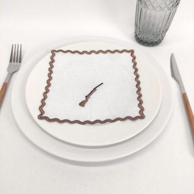 Pratos brancos com guardanapo branco bordado castanho e talheres com cabo de madeira e copo cinzento