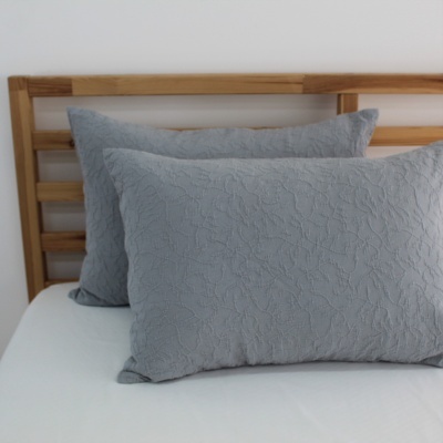 Duas almofadas cinzentas com padrão floral numa cama com cabeceira de madeira clara