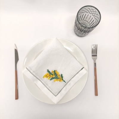 Mesa posta com prato branco, guardanapo bordado, talheres com cabo castanho e copo de vidro com padrão preto