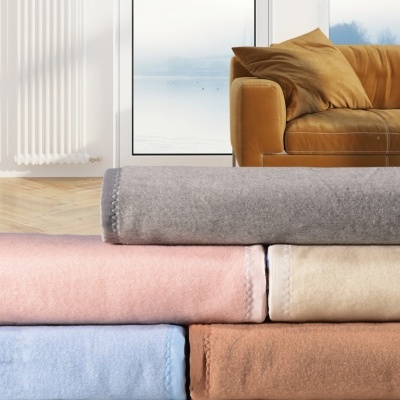 Seis mantas coloridas empilhadas numa sala com sofá castanho claro