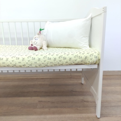 Cama de criança branca com colchão amarelo e peluche sobre almofada branca