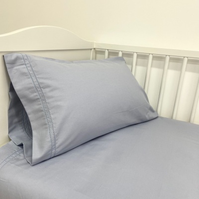 Lençol azul claro com fronha costurada em cama branca de metal