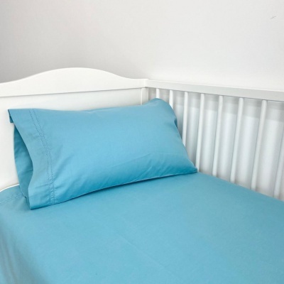 Cama de bebé branca com roupa de cama azul clara e fronha com bordados