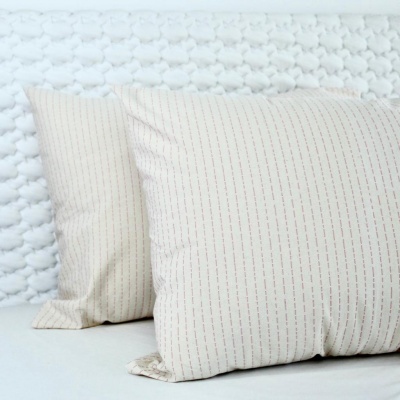 Duas almofadas bege com linhas vermelhas verticais sobre superfície clara e fundo branco texturizado