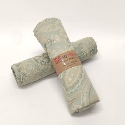 Tecidos enrolados com padrão floral verde-água e bege e etiqueta AGTEX Home Textiles