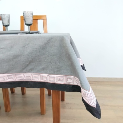 Toalha de mesa cinza com padrão geométrico nas bordas sobre mesa de madeira com copos de vidro texturizados