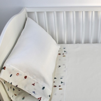 Cama de bebé branca com roupa de cama branca e fronha com pequenos padrões coloridos