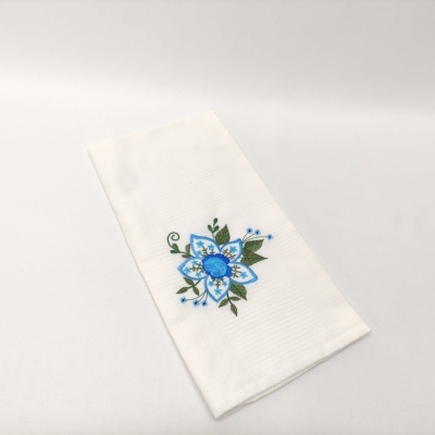 Toalha branca com bordado azul e verde sobre superfície branca