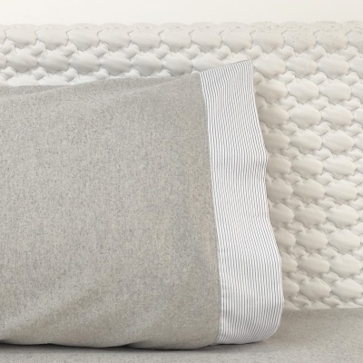 Travesseiro cinzento com faixa riscada branca encostado a fundo texturizado branco