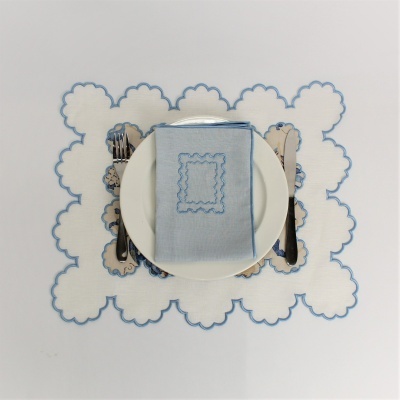 Conjunto de prato branco e talheres sobre toalha branca bordada em azul com guardanapo azul claro bordado.