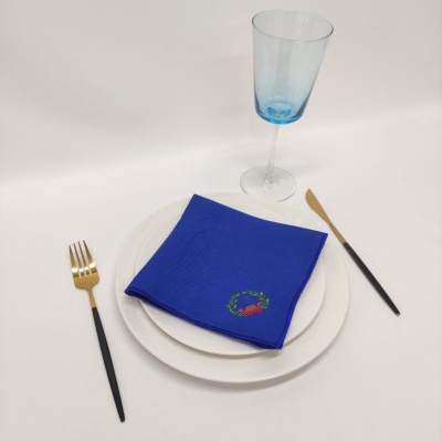 Conjunto de pratos brancos com guardanapo azul bordado, talheres com cabo preto e copo azul translúcido