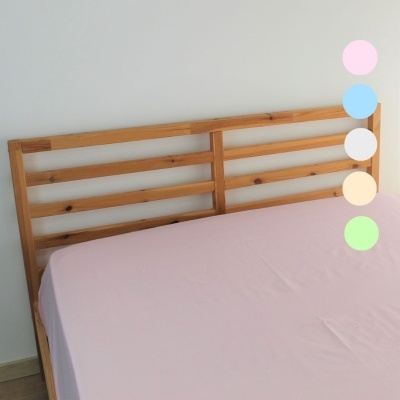 Cama de madeira clara com lençol rosa claro, cabeceira ripada