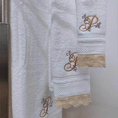 Conjunto de toalhas brancas com bordado dourado e renda bege penduradas num suporte metálico