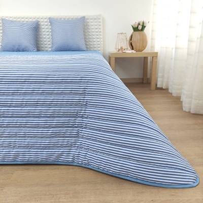 colcha azul e branca às riscas horizontais em cama com almofadas a condizer num quarto com mesa e jarro de flores