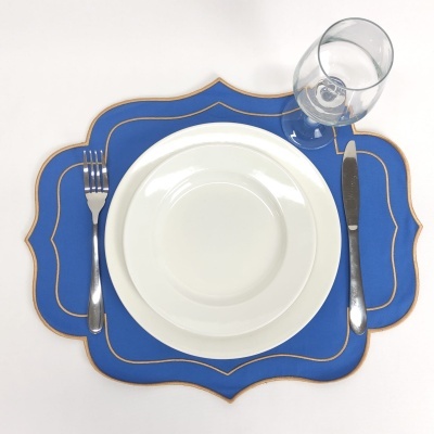 Jogo americano azul com borda dourada, pratos brancos, talheres de metal e copo de vidro