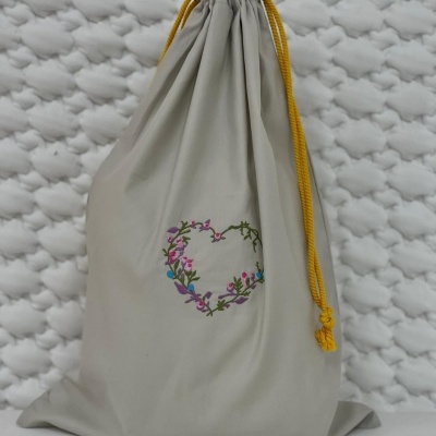 Saco de tecido cinzento claro com cordões amarelos e bordado de coração floral