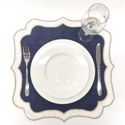 Conjunto de mesa posto com pratos brancos, talheres prateados, copo de vidro e bases para pratos azul escuro e bege