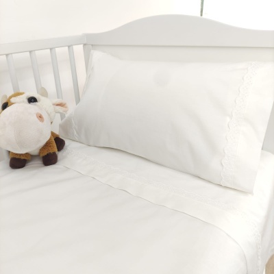 Cama branca com lençol e fronha brancos bordados e peluche de vaca