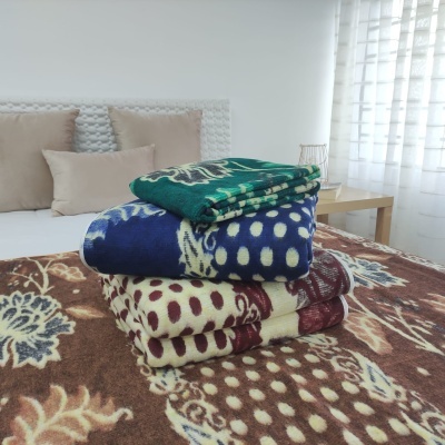 Três mantas dobradas com padrões de bolinhas e florais sobre uma cama com edredão castanho com motivos florais