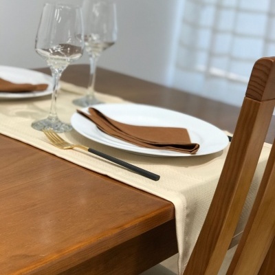 Mesa posta com pratos brancos, guardanapos castanhos, copos de vinho e talheres com cabo preto