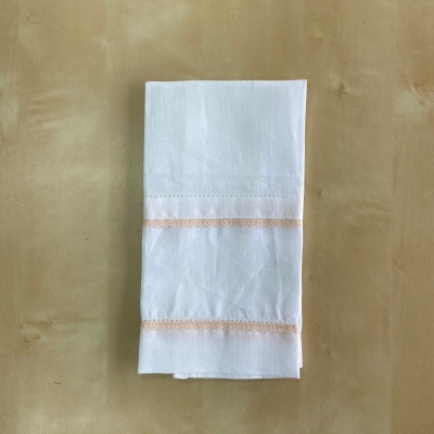 Guardanapo de tecido branco com bordado rosa claro sobre superfície bege