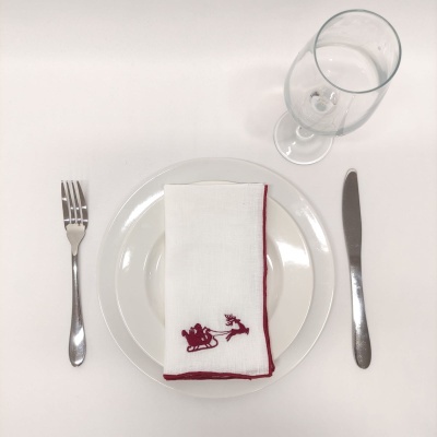Conjunto de mesa com prato branco, talheres metálicos, copo transparente e guardanapo branco com bordado vermelho