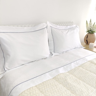 Conjunto de roupa de cama branco com detalhes azuis e edredão creme em cama moderna com mesa e decoração