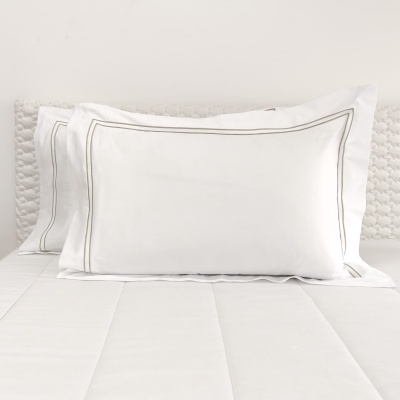 Almofadas brancas com linhas cinza finas sobre cama branca com cabeceira texturizada